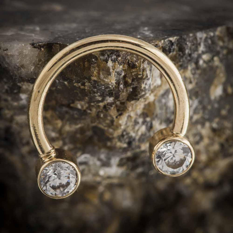 14k yellow gold CZ circular barbell resting against rough stone surface, lifestyle detail shot