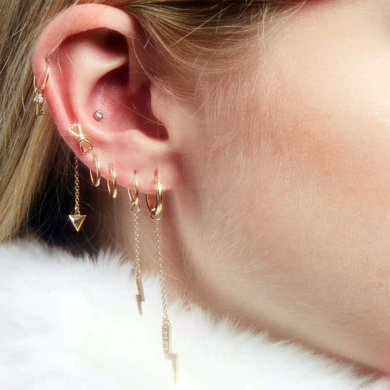 Gold key diamond charm worn on helix piercing in a curated ear with multiple gold hoops