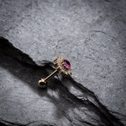 14K yellow gold flower cartilage barbell with ruby center resting in slate rock crevice, side angle