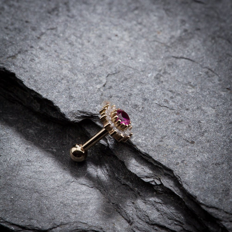 14K yellow gold flower cartilage barbell with ruby center resting in slate rock crevice, side angle