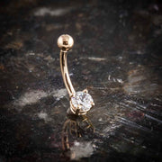 14k rose gold CZ belly ring angled on dark stone surface showing curved barbell profile