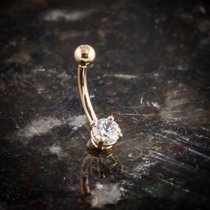 14k rose gold CZ belly ring angled on dark stone surface showing curved barbell profile