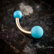14k yellow gold turquoise double ball navel ring resting on dark stone surface