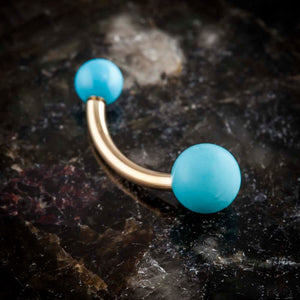 14k yellow gold turquoise double ball navel ring resting on dark stone surface