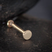 Close-up of 14K rose gold 2.5mm disc flat back labret on dark stone surface, disc end facing forward