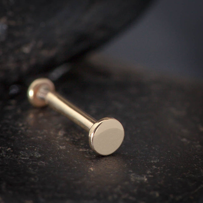 Close-up of 14K rose gold 2.5mm disc flat back labret on dark stone surface, disc end facing forward