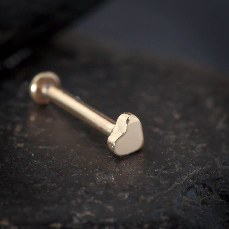 Close-up of 2mm solid gold artisan heart labret stud on dark stone surface showing handcrafted texture