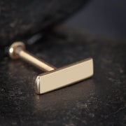 Close-up of 14K yellow gold 7mm bar labret stud on dark textured surface showing polish