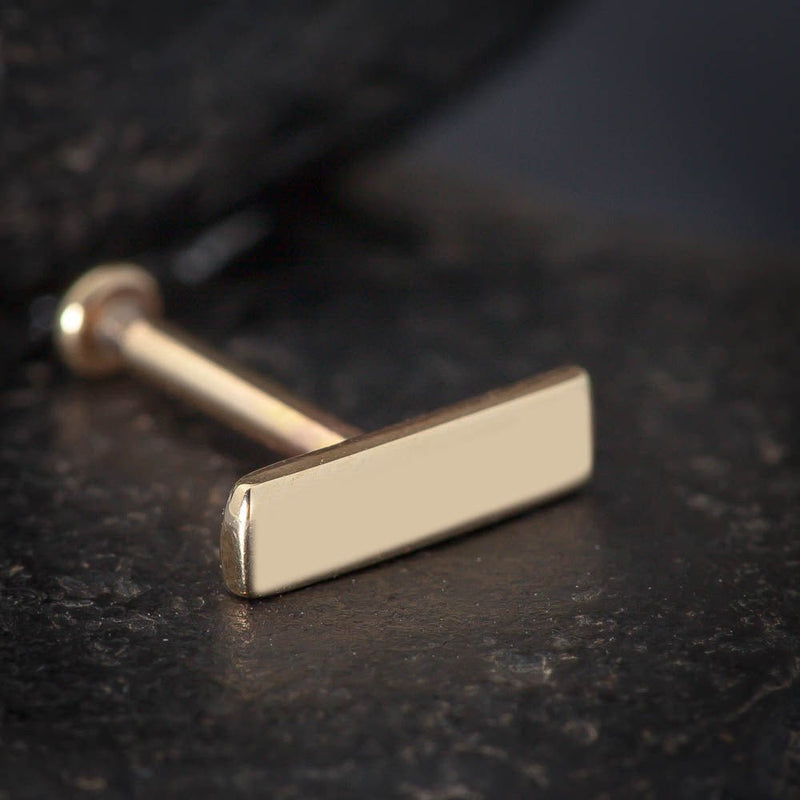 Close-up of 14K yellow gold 7mm bar labret stud on dark textured surface showing polish