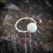 Twisted captive bead ring with white opal bead resting on dark natural stone surface for texture contrast