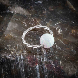 Twisted captive bead ring with white opal bead resting on dark natural stone surface for texture contrast