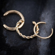 Two 14K gold twisted band ear cuffs layered together on dark stone surface