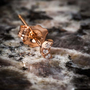 14k rose gold crescent moon diamond stud earring resting on natural stone surface, angled view