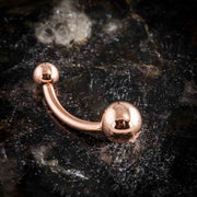 14k rose gold double ball belly ring on dark granite surface, side profile showing curved barbell