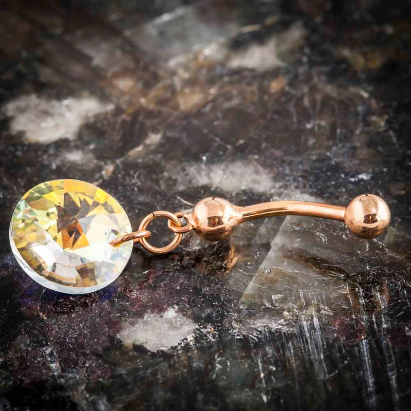 14k rose gold Swarovski rivoli belly ring laid flat on dark stone surface, angled lifestyle shot
