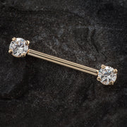 14k rose gold straight barbell with clear round CZ ends resting on dark stone surface