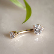 14k yellow gold heart CZ belly ring resting on marble surface beside a green leaf