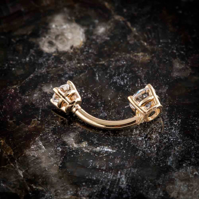 14k yellow gold double gem belly ring laid flat on stone surface, showing curved barbell profile