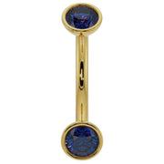 Close-up of 14k yellow gold curved barbell highlighting deep blue sapphire bezel ends