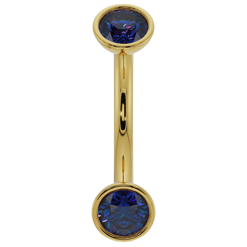 Close-up of 14k yellow gold curved barbell highlighting deep blue sapphire bezel ends