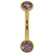 Close-up of 14K yellow gold curved barbell highlighting larger bezel-set pink sapphire ends