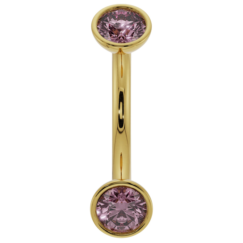 Close-up of 14K yellow gold curved barbell highlighting larger bezel-set pink sapphire ends