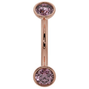 Close-up of 14K rose gold curved barbell with larger bezel-set pink sapphire ends, front view