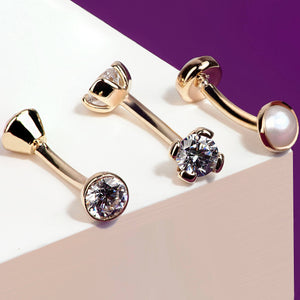 Assorted 14k rose gold curved barbells with CZ and pearl stones shown as style reference on geometric surface