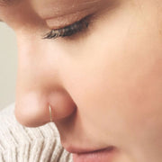 Thin gold seam ring hoop worn in a nostril piercing, close-up profile view showing minimal dainty fit