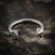 14K white gold spike circular barbell resting on dark rock, angled side view