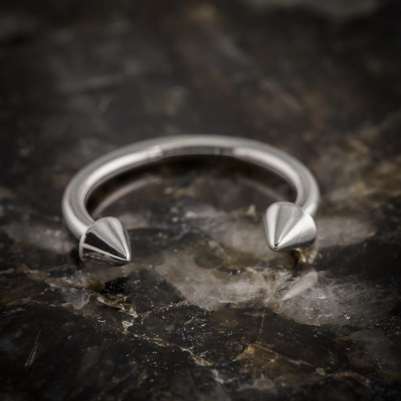 14K white gold spike circular barbell resting on dark rock, angled side view