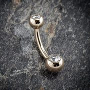 14k yellow gold double clear CZ navel ring resting on stone surface, angled lifestyle shot