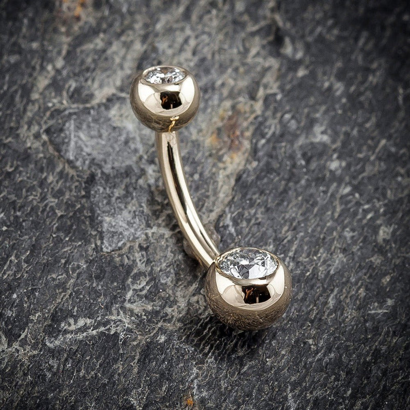 14k yellow gold double clear CZ navel ring resting on stone surface, angled lifestyle shot