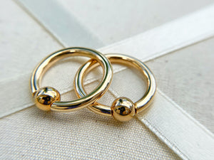Pair of 14k yellow gold captive bead nipple rings resting on linen textile, angled close-up