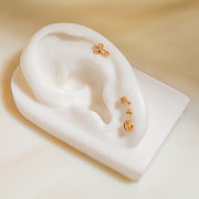 Diamond cross flat back stud in 14k gold shown in helix piercing on white ceramic ear prop, styled look