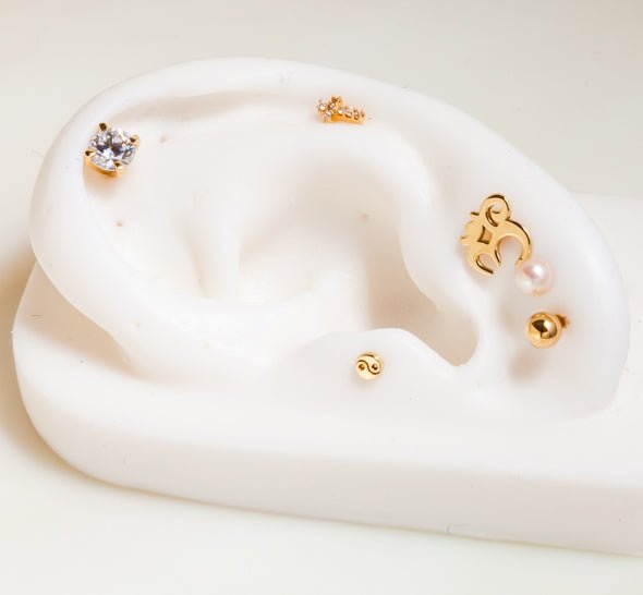 14k gold yin yang flat back stud displayed on white ear mannequin alongside other dainty gold studs