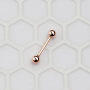 Small 14k rose gold straight barbell on hexagon tile surface showing compact size for cartilage or tongue