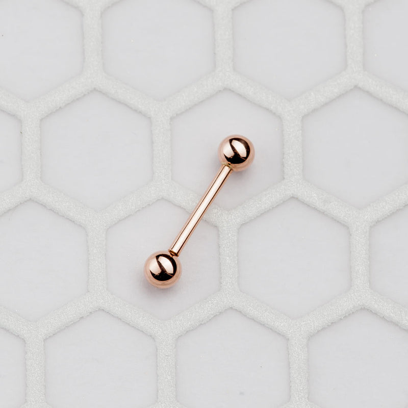 Small 14k rose gold straight barbell on hexagon tile surface showing compact size for cartilage or tongue