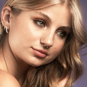 Gold circular barbell worn as a septum piercing on a female model, shown with ear piercings