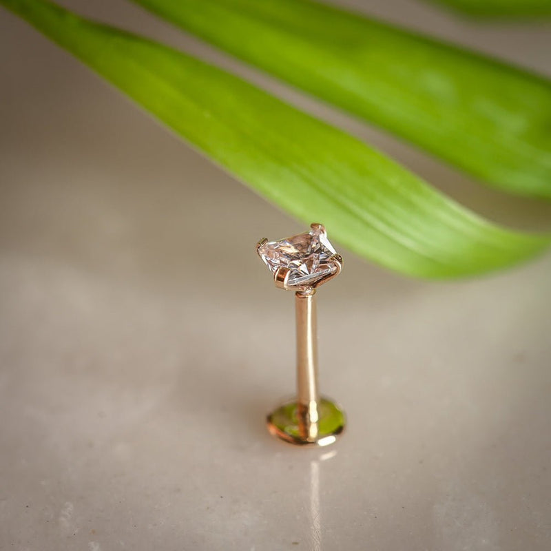 14K rose gold square CZ flat back labret standing upright with tropical leaf background