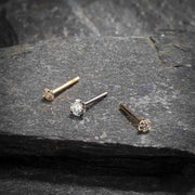 Three 3mm CZ straight post nose rings in yellow and white gold shown on textured stone surface