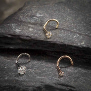 Three 14k gold CZ twist nose rings in yellow, white, and rose gold displayed on dark stone surface