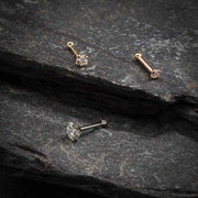 14k gold CZ nose bone and straight post styles in yellow, white, and rose gold on dark stone surface