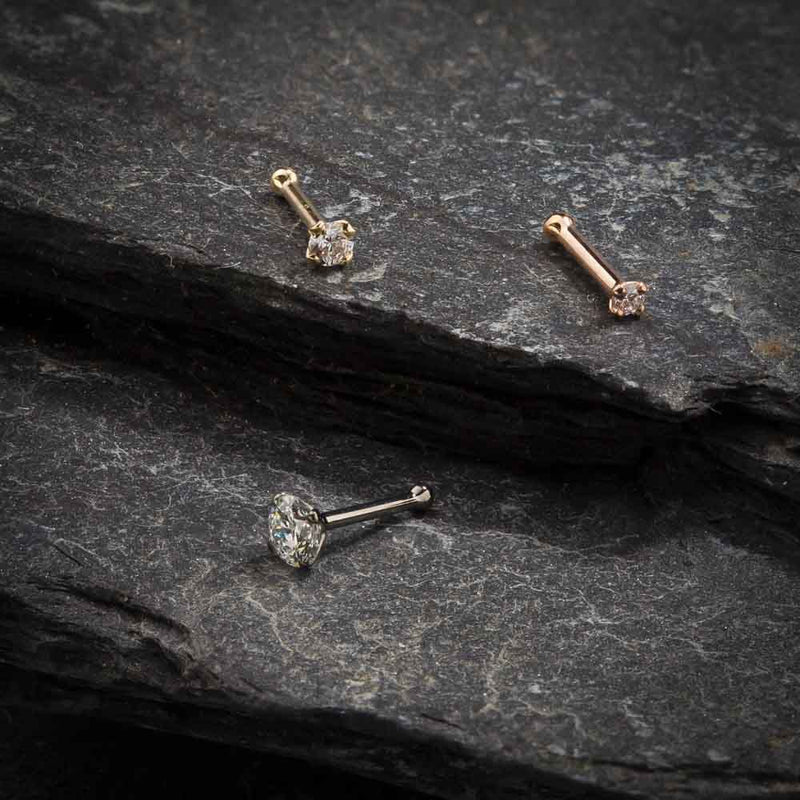 14k gold CZ nose bone and straight post styles in yellow, white, and rose gold on dark stone surface