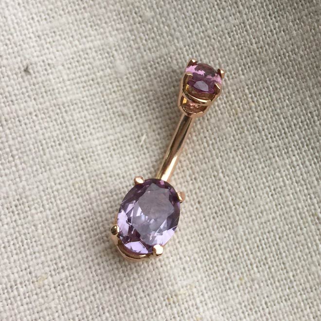 14k rose gold belly ring with purple oval CZ stones on linen fabric, angled view