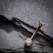 14k rose gold diamond belly ring laid flat on textured slate stone, full barbell length visible