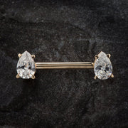 14k yellow gold industrial barbell with clear pear-cut CZ ends on dark stone surface, front view