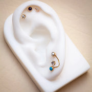 14k gold CZ prong-set flat back stud styled on white ear display with mixed piercing jewelry curation