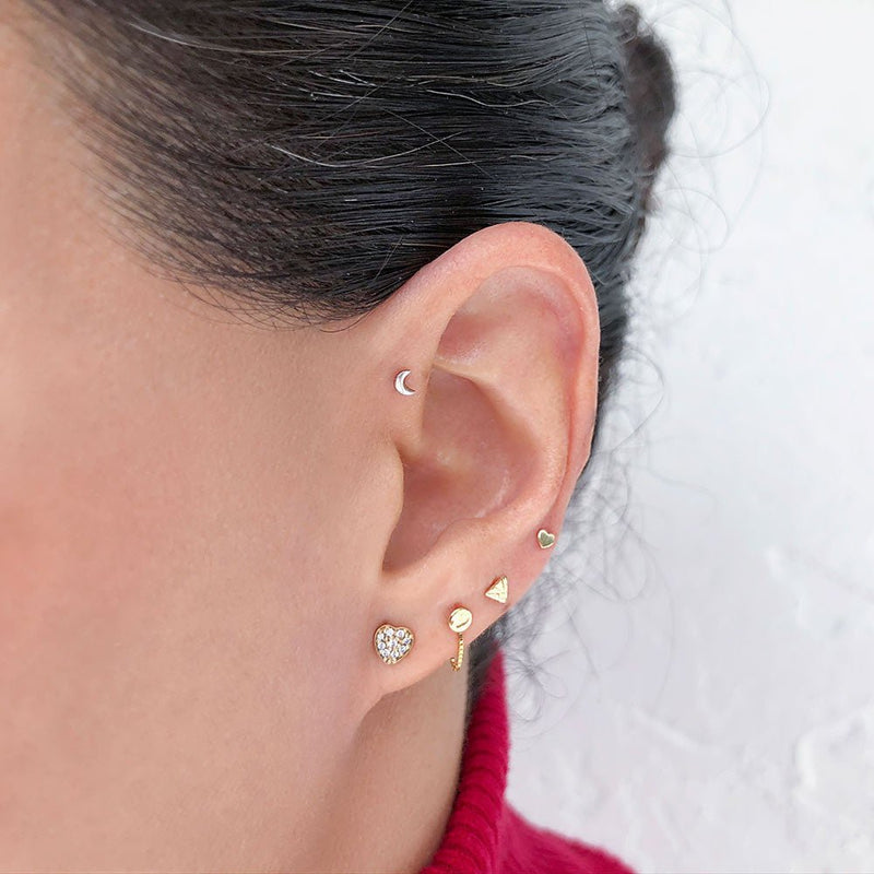 Diamond paved heart stud earring worn in lobe piercing as part of a stacked gold ear party