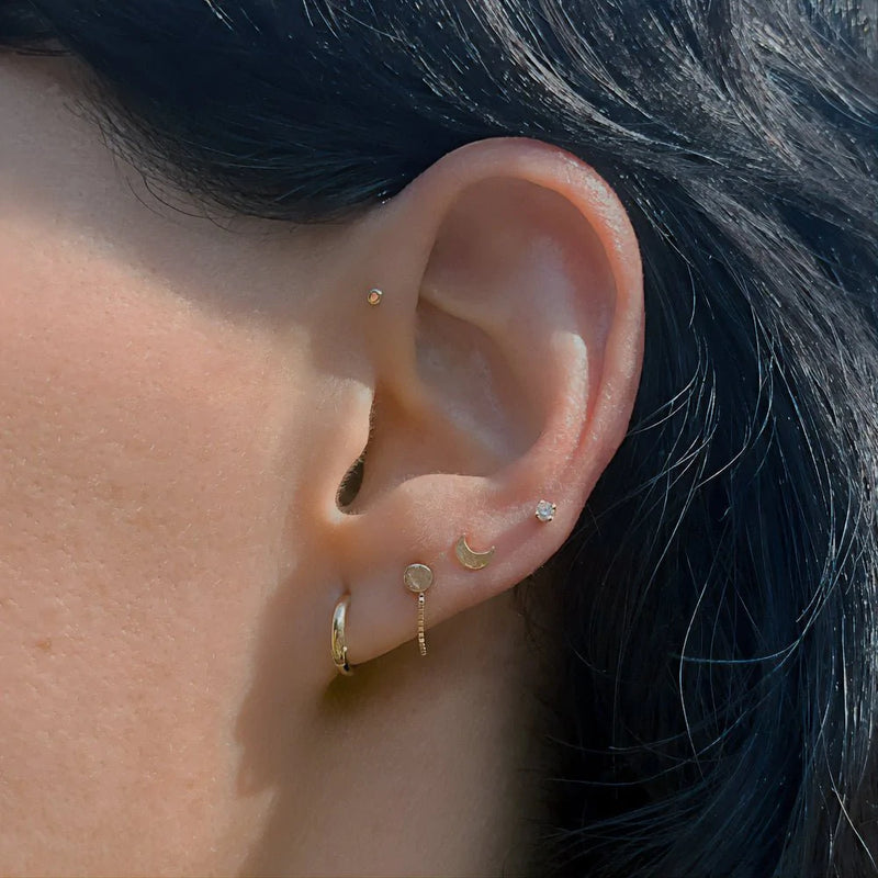 14k gold CZ flat back stud worn in helix piercing on dark-haired model with layered ear stack